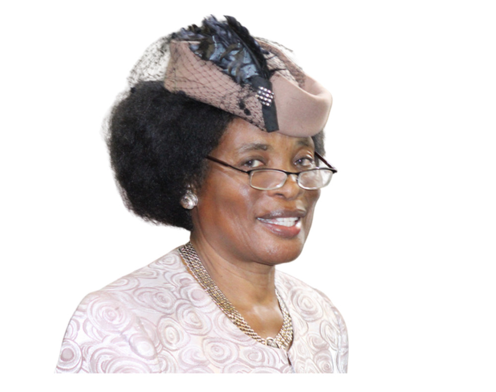 Sarah Mutua smiling, wearing glasses and a pale pink outfit